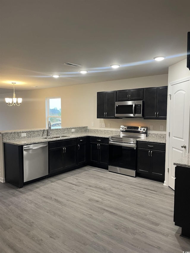 kitchen with appliances with stainless steel finishes, light wood-type flooring, a notable chandelier, and sink