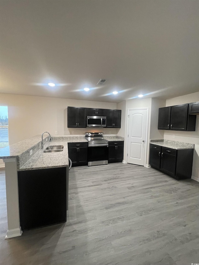 kitchen with sink, light wood-type flooring, appliances with stainless steel finishes, light stone counters, and kitchen peninsula