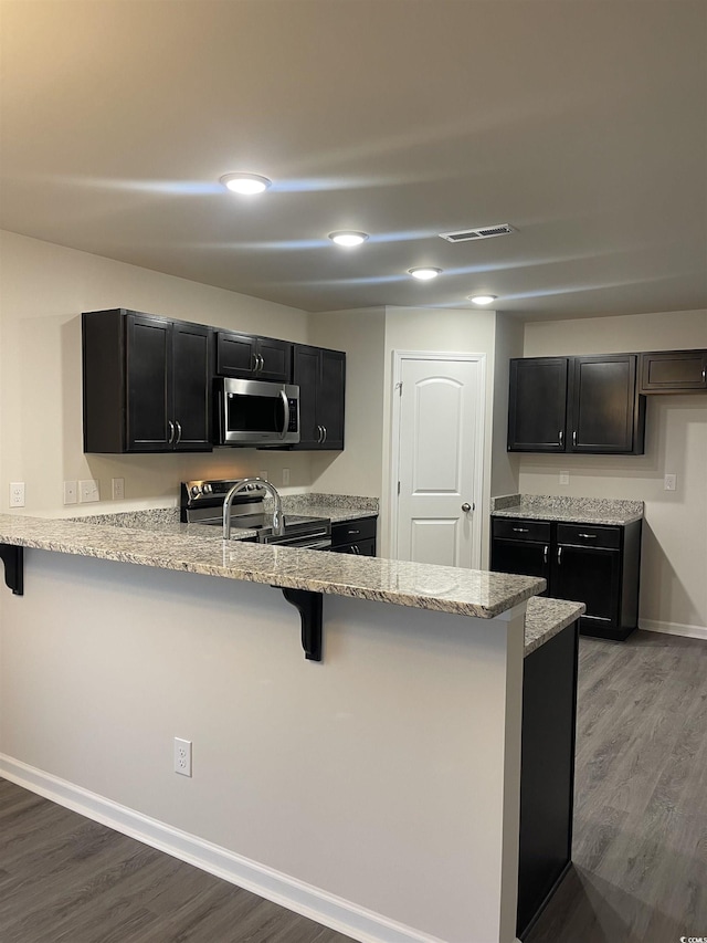 kitchen with a breakfast bar area, kitchen peninsula, dark hardwood / wood-style flooring, and appliances with stainless steel finishes