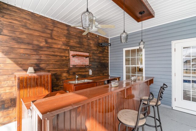 bar featuring pendant lighting, wood walls, and sink