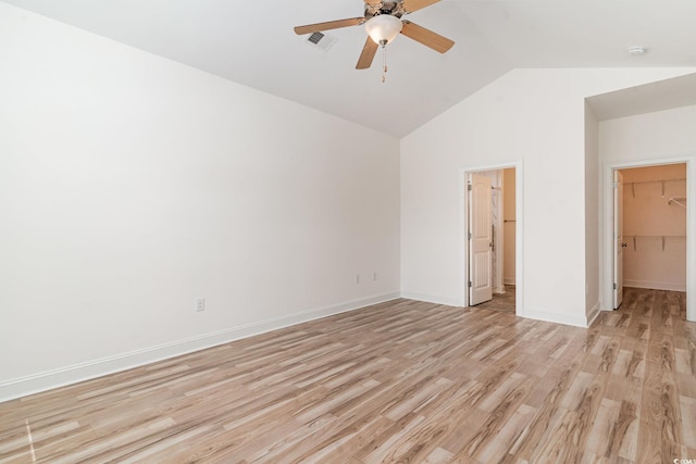 unfurnished bedroom featuring ceiling fan, lofted ceiling, a walk in closet, a closet, and light wood-type flooring