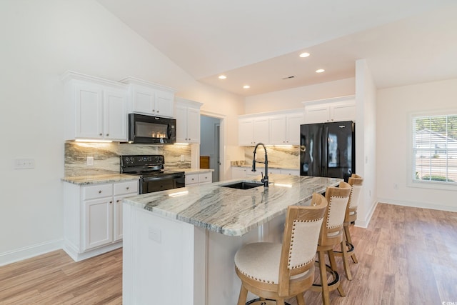 kitchen featuring black appliances, white cabinetry, sink, and an island with sink