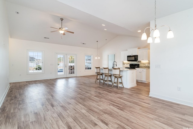 unfurnished living room with french doors, ceiling fan with notable chandelier, sink, high vaulted ceiling, and light hardwood / wood-style flooring