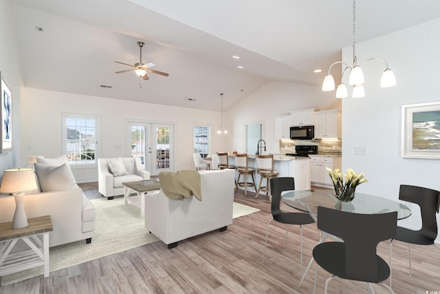 living room with light wood-type flooring, french doors, ceiling fan with notable chandelier, and high vaulted ceiling