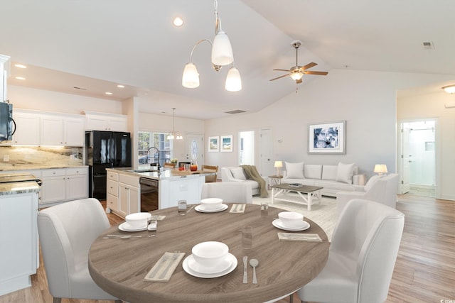 dining area with ceiling fan with notable chandelier, light hardwood / wood-style floors, sink, and vaulted ceiling