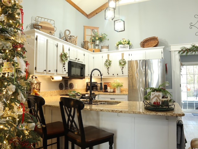 kitchen with stainless steel refrigerator, white cabinetry, light stone countertops, and lofted ceiling