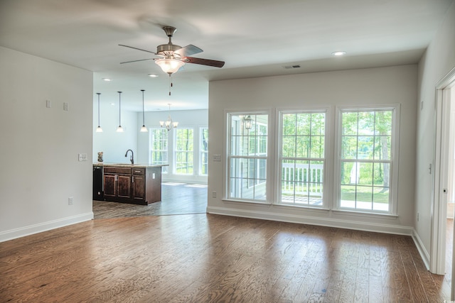 unfurnished living room with sink, ceiling fan with notable chandelier, and dark hardwood / wood-style floors