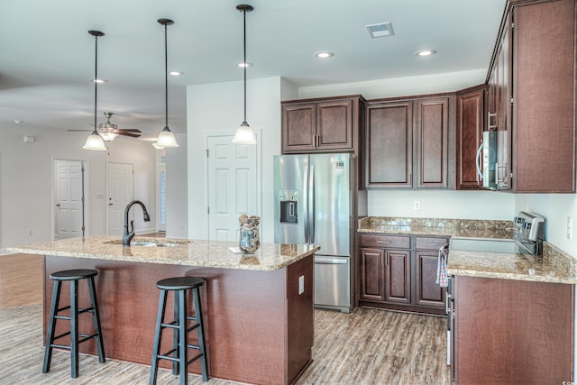 kitchen featuring ceiling fan, stainless steel appliances, pendant lighting, a kitchen island with sink, and light wood-type flooring