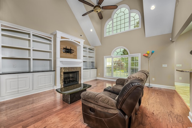 living room featuring ceiling fan, a high end fireplace, high vaulted ceiling, and light wood-type flooring