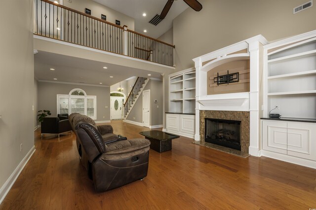 living room with ornamental molding, built in shelves, ceiling fan, wood-type flooring, and a high ceiling