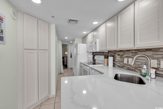 kitchen with light stone countertops, sink, a textured ceiling, white appliances, and light tile patterned flooring