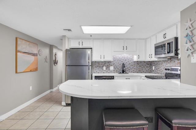 kitchen featuring backsplash, kitchen peninsula, appliances with stainless steel finishes, white cabinetry, and a breakfast bar area