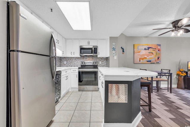 kitchen featuring kitchen peninsula, a kitchen breakfast bar, stainless steel appliances, white cabinets, and light hardwood / wood-style floors