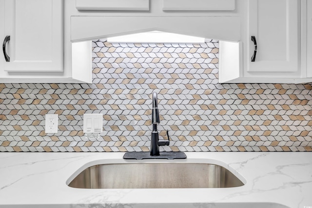 kitchen featuring light stone countertops, white cabinetry, and sink