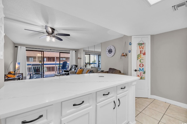 kitchen featuring white cabinets, ceiling fan, light stone countertops, and light tile patterned floors