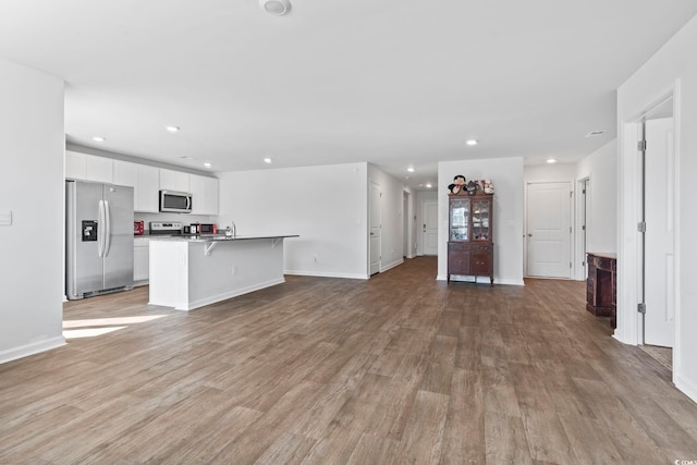 kitchen with a kitchen breakfast bar, a center island with sink, light wood-type flooring, and appliances with stainless steel finishes