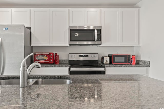 kitchen featuring white cabinets, appliances with stainless steel finishes, and dark stone counters