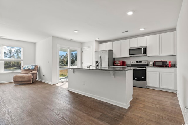 kitchen featuring a kitchen breakfast bar, dark hardwood / wood-style flooring, stainless steel appliances, and a kitchen island with sink