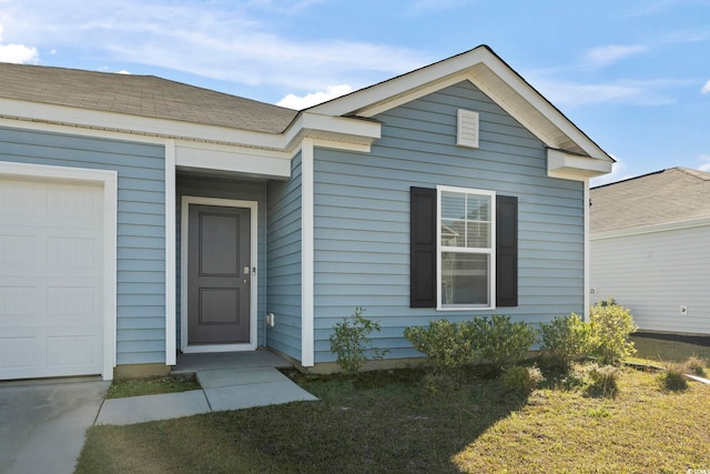 doorway to property with a garage and a lawn