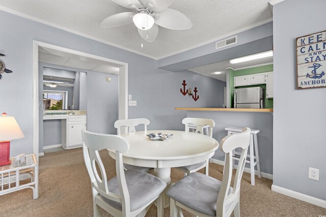 carpeted dining space featuring a textured ceiling, ceiling fan, ornamental molding, and sink