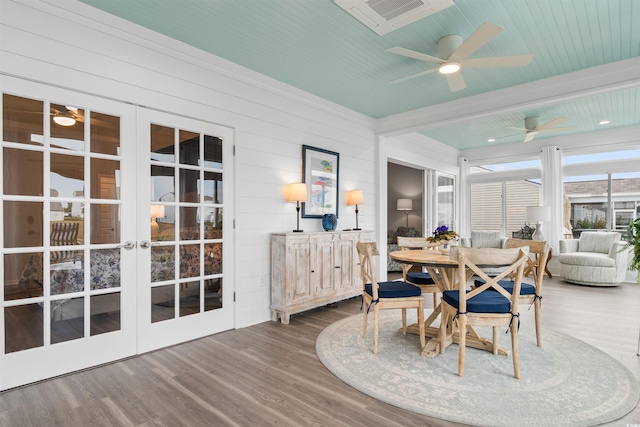 dining area featuring hardwood / wood-style floors, wooden walls, french doors, beam ceiling, and ceiling fan