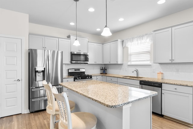 kitchen featuring a kitchen island, stainless steel appliances, sink, hanging light fixtures, and light stone counters