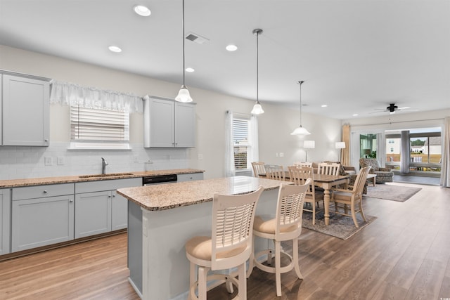 kitchen with hanging light fixtures, decorative backsplash, a kitchen breakfast bar, sink, and a kitchen island