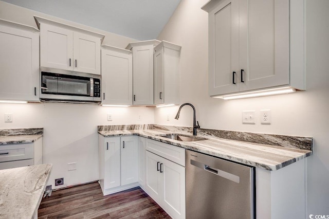 kitchen with white cabinets, light stone counters, a sink, appliances with stainless steel finishes, and dark wood-style flooring