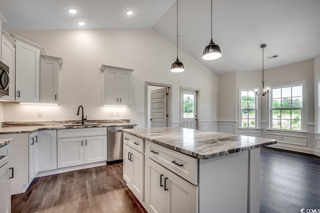 kitchen with a wainscoted wall, dark wood-style floors, a sink, light stone countertops, and appliances with stainless steel finishes
