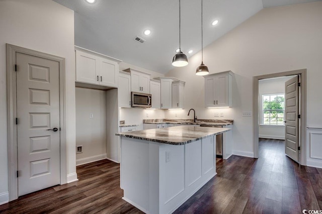 kitchen featuring a sink, stainless steel microwave, dark wood finished floors, visible vents, and a kitchen island