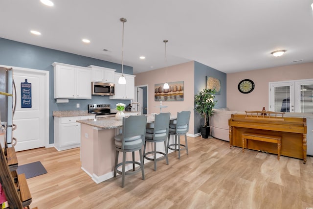 kitchen featuring white cabinets, decorative light fixtures, stainless steel appliances, and a kitchen island with sink