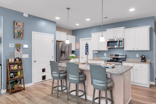 kitchen featuring stainless steel appliances, pendant lighting, a center island with sink, light hardwood / wood-style floors, and white cabinetry