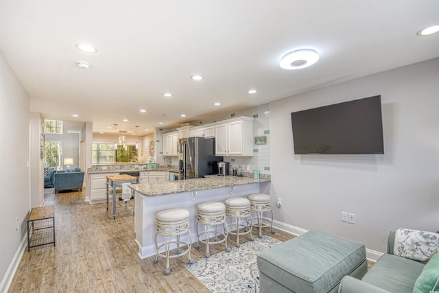 kitchen with kitchen peninsula, stainless steel fridge, a kitchen bar, light hardwood / wood-style flooring, and white cabinets