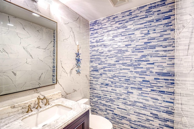 bathroom featuring vanity, toilet, and tile walls