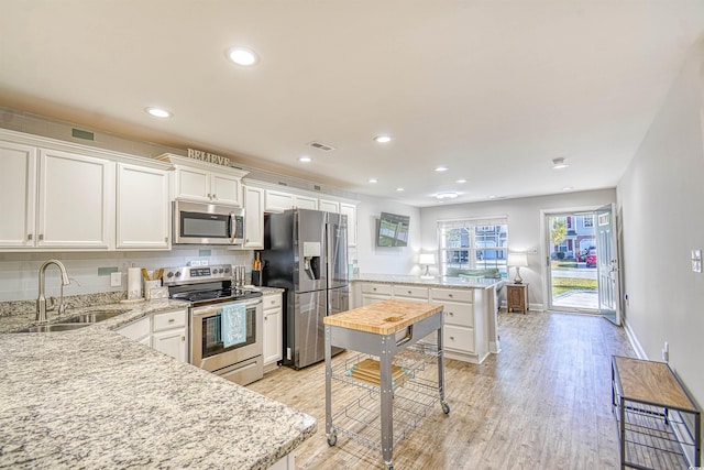 kitchen featuring tasteful backsplash, stainless steel appliances, sink, light hardwood / wood-style flooring, and white cabinetry