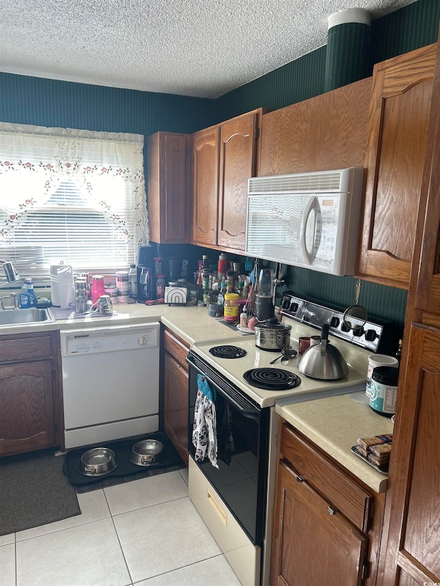 kitchen featuring light tile patterned floors, white appliances, a textured ceiling, and sink