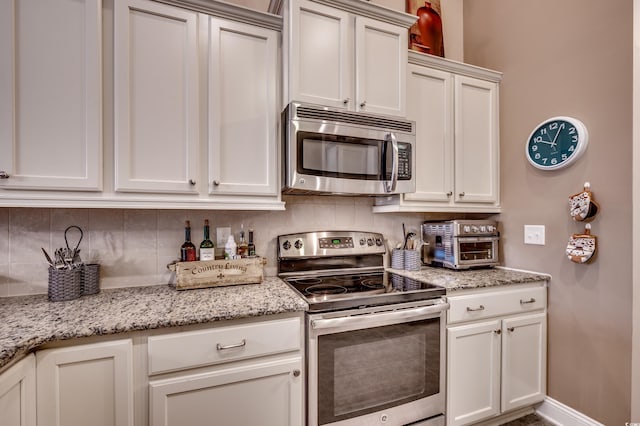 kitchen featuring tasteful backsplash, light stone counters, white cabinets, and appliances with stainless steel finishes