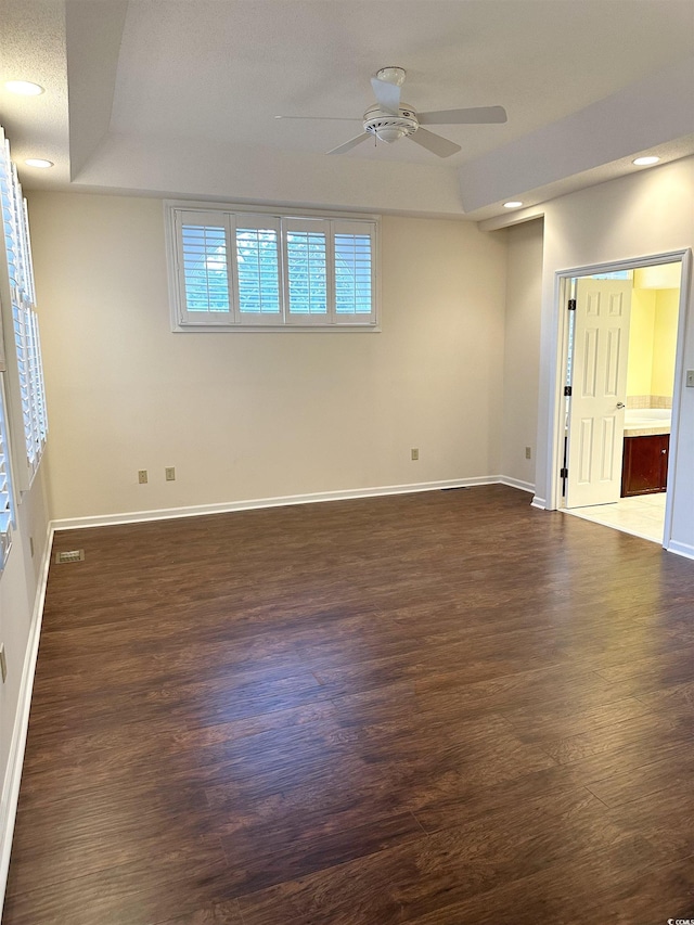 empty room with a tray ceiling, dark wood-type flooring, and ceiling fan