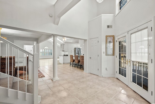 tiled foyer entrance featuring french doors, ceiling fan, beamed ceiling, a towering ceiling, and decorative columns