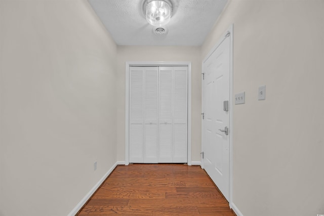 hall featuring baseboards, visible vents, a textured ceiling, and wood finished floors