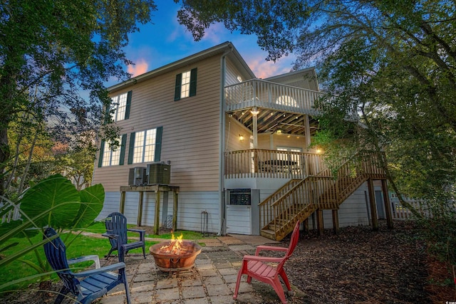 back house at dusk featuring a wooden deck, a patio, a fire pit, and cooling unit