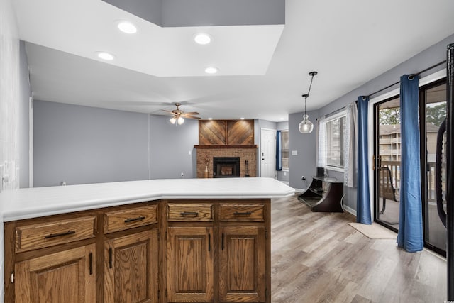 kitchen with pendant lighting, a brick fireplace, ceiling fan, light hardwood / wood-style floors, and kitchen peninsula