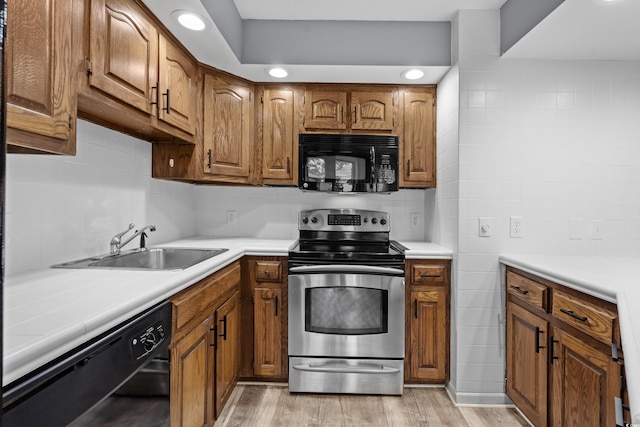 kitchen featuring sink, light wood-type flooring, tasteful backsplash, and black appliances