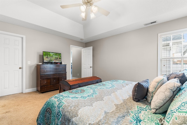 bedroom with a raised ceiling, visible vents, light carpet, ceiling fan, and baseboards