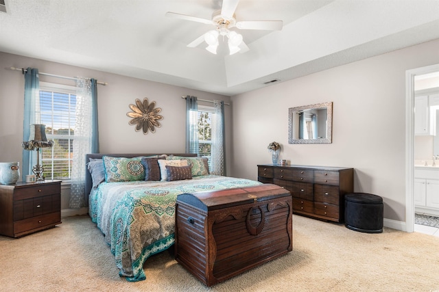 bedroom with a raised ceiling, light colored carpet, visible vents, ensuite bathroom, and baseboards