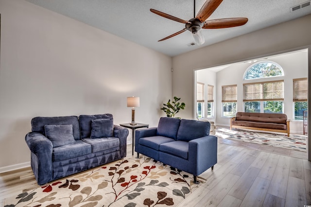 living room featuring ceiling fan, light hardwood / wood-style floors, and a textured ceiling