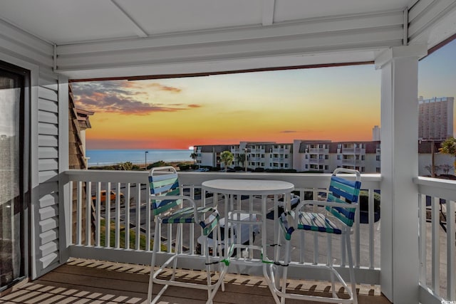 balcony at dusk featuring a water view