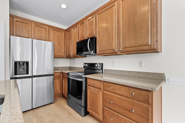 kitchen with appliances with stainless steel finishes, light stone countertops, and light wood-type flooring