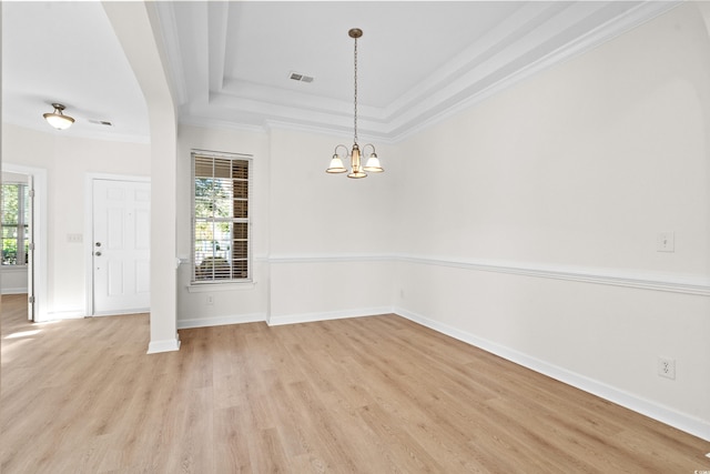 empty room with ornamental molding, a tray ceiling, light hardwood / wood-style flooring, and a notable chandelier