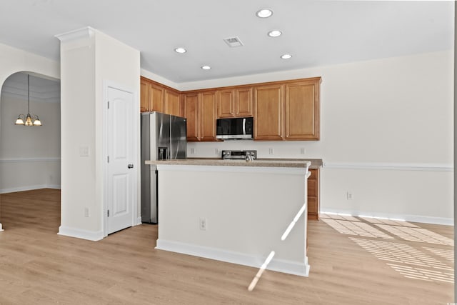 kitchen featuring appliances with stainless steel finishes, hanging light fixtures, a center island with sink, a chandelier, and light wood-type flooring